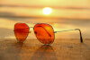 red lens sunglasses on sand near sea at sunset selective focus photography